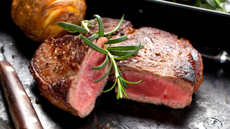 Steak cut in half with rosemary on black plate