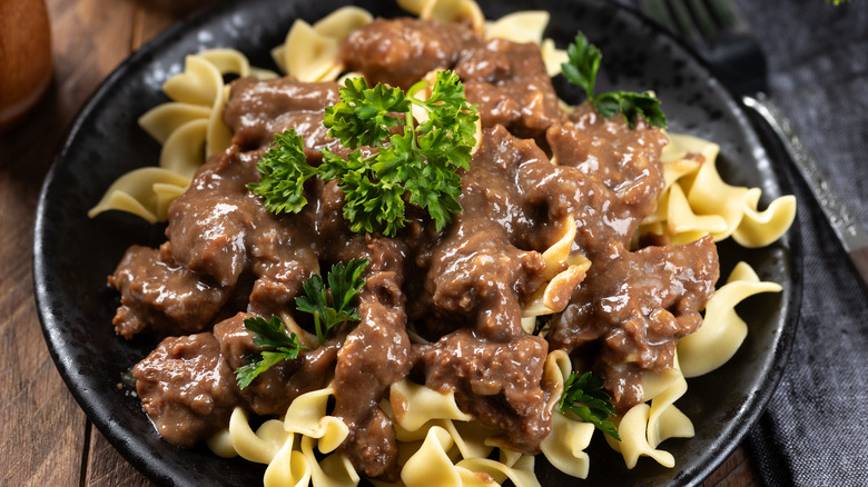 Beef stroganoff with egg noodles garnished with parsley on a black dinner plate