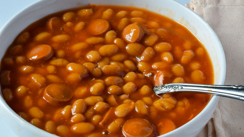 white bowl of beans with sliced hot dogs