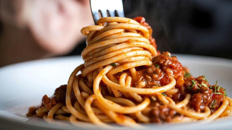 spaghetti twirled around fork from plate with spaghetti and meat sauce