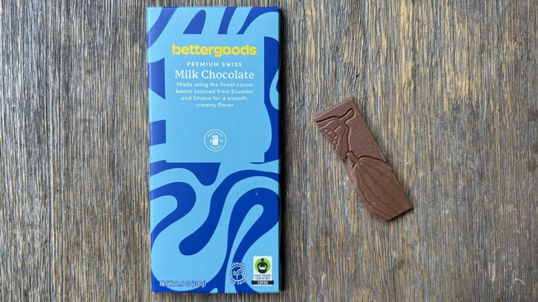 Wrapped bettergoods milk chocolate bar on table with rectangular piece adjacent, adorned with cacao pods impression
