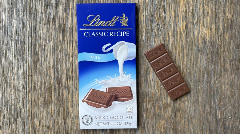 Wrapped Lindt milk chocolate bar on table with long rectangular piece adjacent, consisting of five sections with Lindt logo