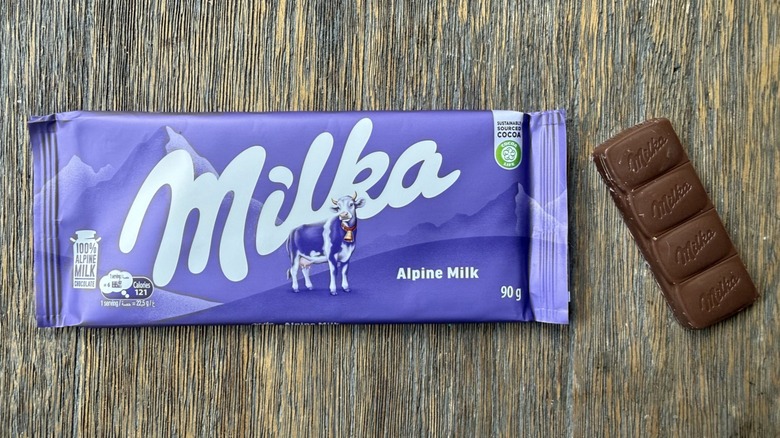 Wrapped Milka alpine milk chocolate bar on table with long rectangular piece adjacent, consisting of four sections