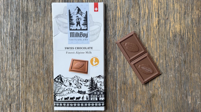 Wrapped MilkBoy milk chocolate bar on table with rectangular piece adjacent, consisting of two large sections adorned with cacao pod impressions