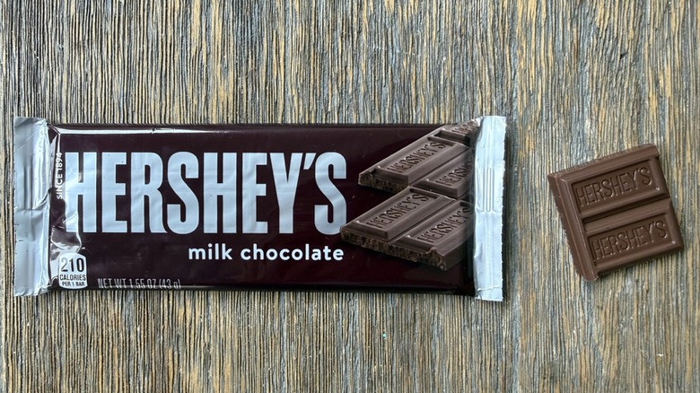 Wrapped Hershey's milk chocolate bar on table with rectangular piece adjacent, consisting of two sections