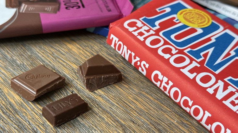 Three pieces of milk chocolate on table alongside wrapped chocolate bars from different brands