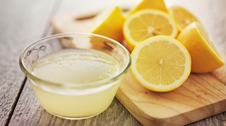 Lemon juice in glass bowl with halved lemons on wooden cutting board