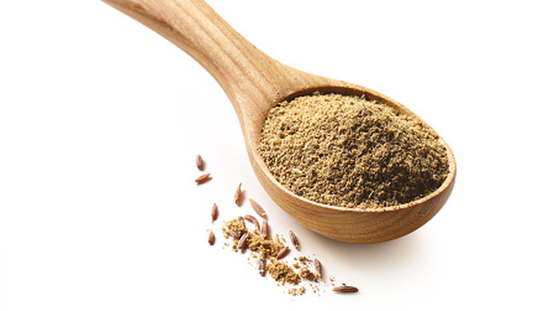 Cumin on wooden spoon on white background