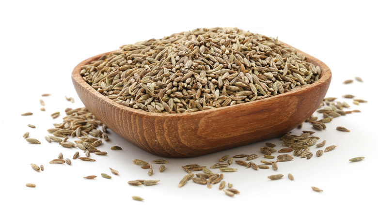 Cumin seeds in wooden bowl on white background