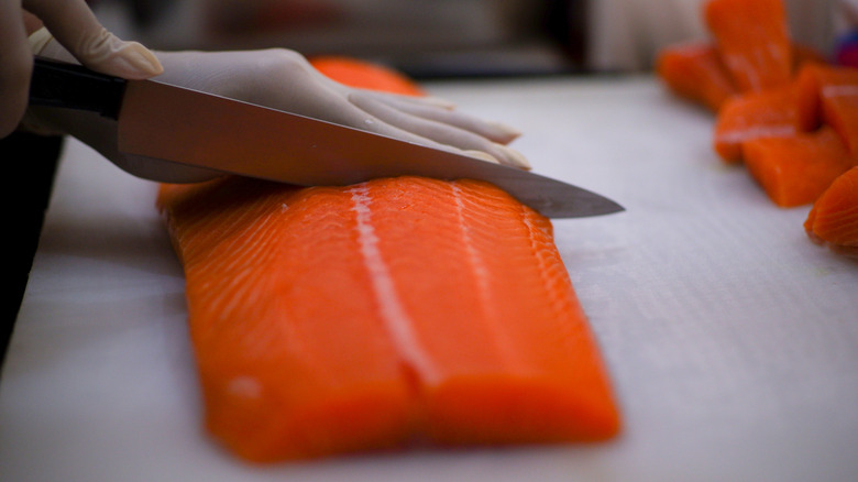hands cutting dry salmon fillet on cutting board