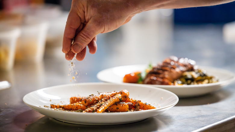 Hand sprinkling seasoning across a pasta dish