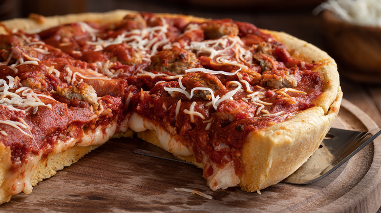 Deep dish pizza with slice missing on wooden cutting board