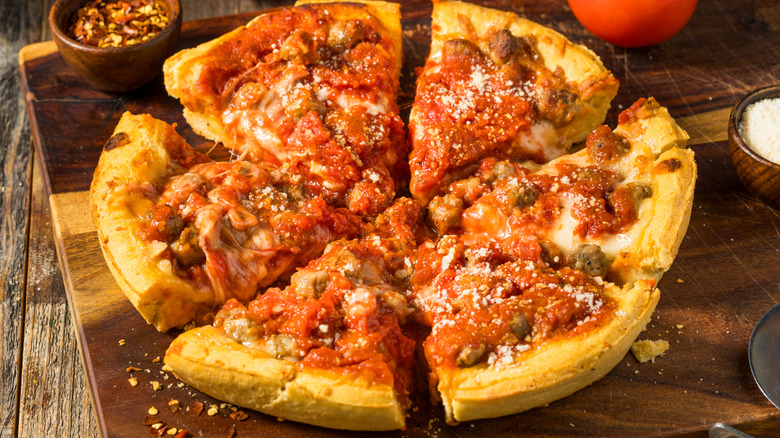 Cut deep dish pizza with various toppings on wooden cutting board