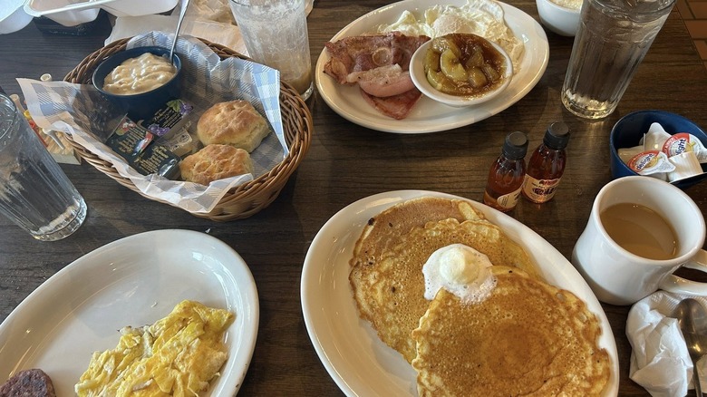A breakfast spread on table at Cracker Barrel, including pancakes, biscuits and gravy, and bacon and eggs