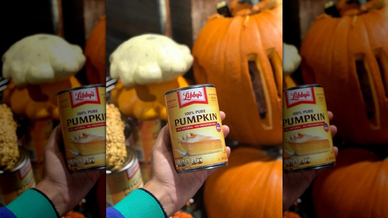 Hand holding can of Libby's pumpkin puree against pumpkin backdrop