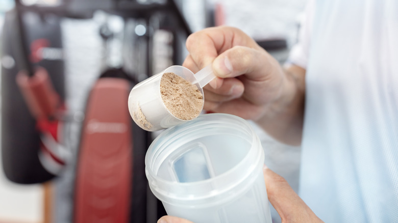 man scooping protein powder into plastic cup