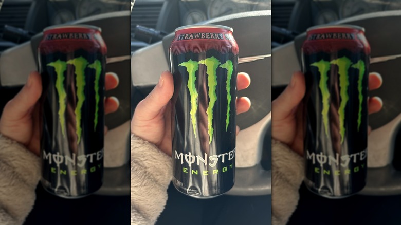 Hand holding can of Monster Energy Strawberry Shot in car