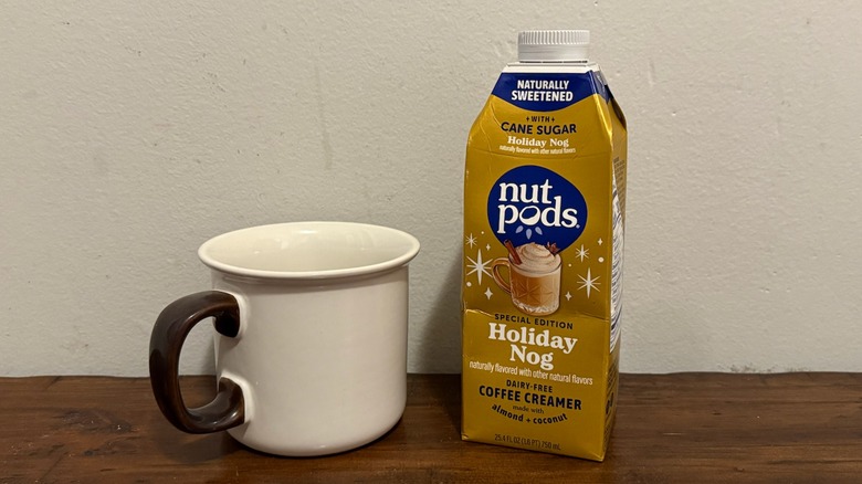 container of Nutpods holiday nog creamer next to a cup of coffee