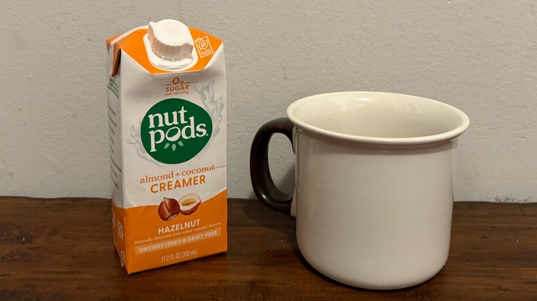 container of Nutpods hazelnut creamer next to a cup of coffee