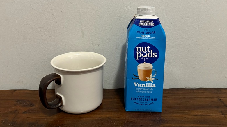 container of Nutpods vanilla creamer next to a cup of coffee