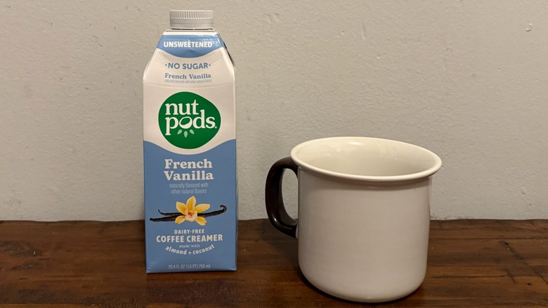 container of Nutpods french vanilla unsweetened creamer next to a cup of coffee