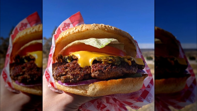 A hand holding a green chile cheeseburger wrapped in checkered paper
