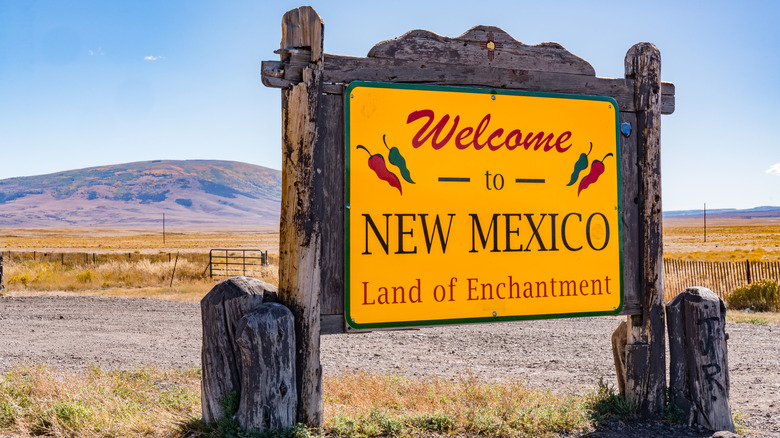 A rustic "Welcome to New Mexico" sign with chile peppers in front of desert mountains
