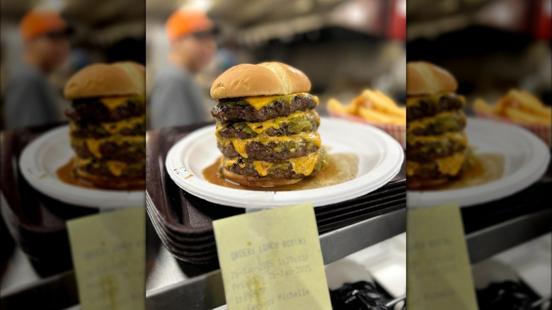 A green chile cheeseburger with four burger patties in a restaurant kitchen window