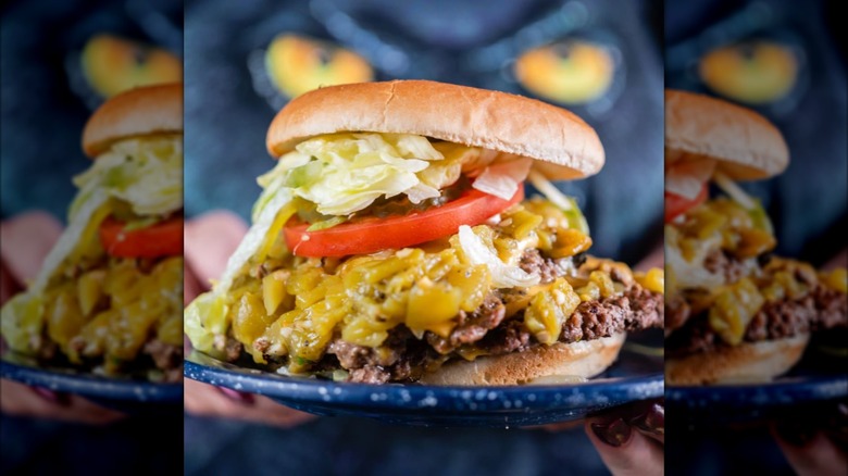 A double green chile cheese burger with lettuce and tomato on a blue plate