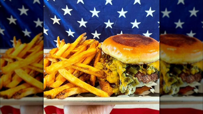 A green chile cheeseburger and fries on a metal tray with an American flag backdrop