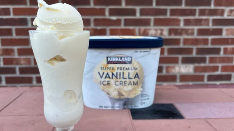 Vanilla ice cream in a sundae glass and an ice cream container in front of a brick background