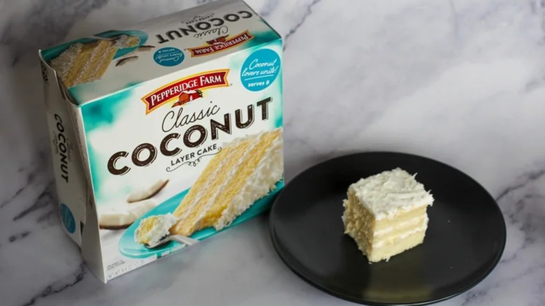 A slice of coconut cake next to its box on a white marble counter