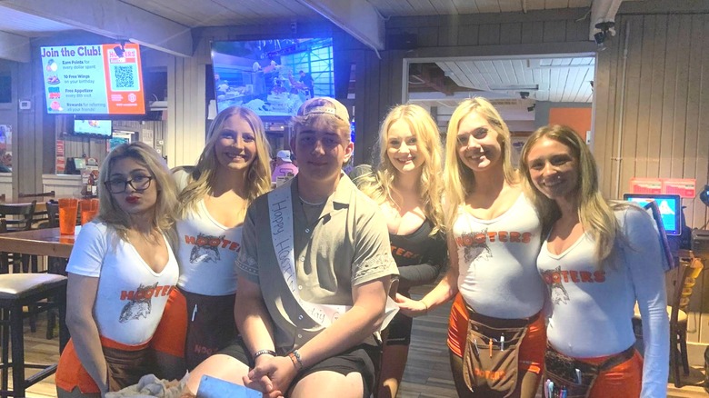 A man dancing with Hooters waitstaff