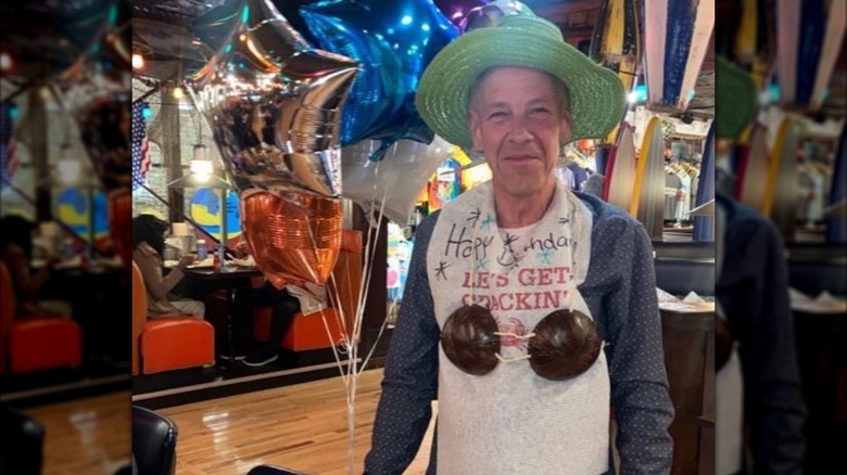 A man wearing a coconut bikini and green hat