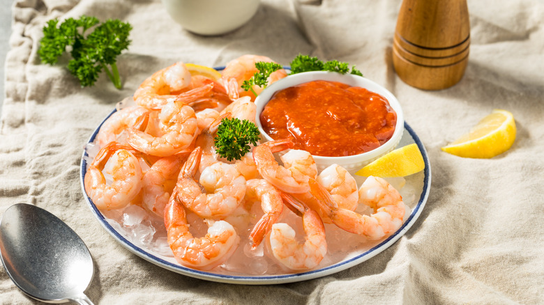 a plate with shrimp on a bed of ice and a bowl of cocktail sauce