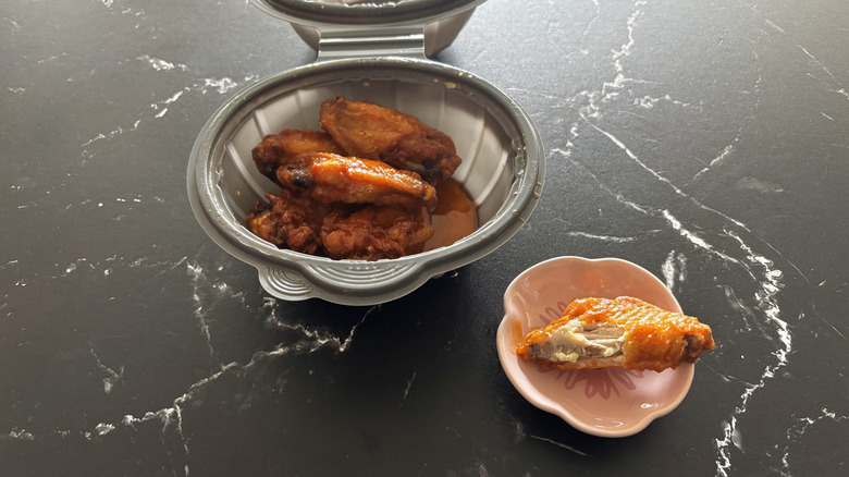 Pizza Hut spicy garlic wings inside a takeout container with one wing on the side