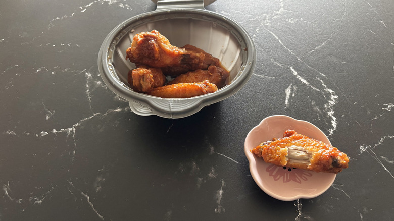 Pizza Hut sweet chili wings inside a takeout container with one wing on a plate next to it