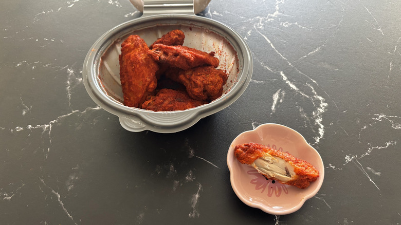 Pizza Hut Nashville hot wings in a plastic container on a dark marble counter and one wing on the side