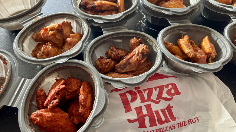 Various containers of wings with Pizza Hut plastic bag assembled on the counter