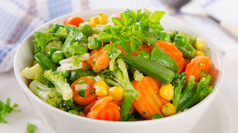Bowl of steamed frozen vegetables, topped with fresh herbs