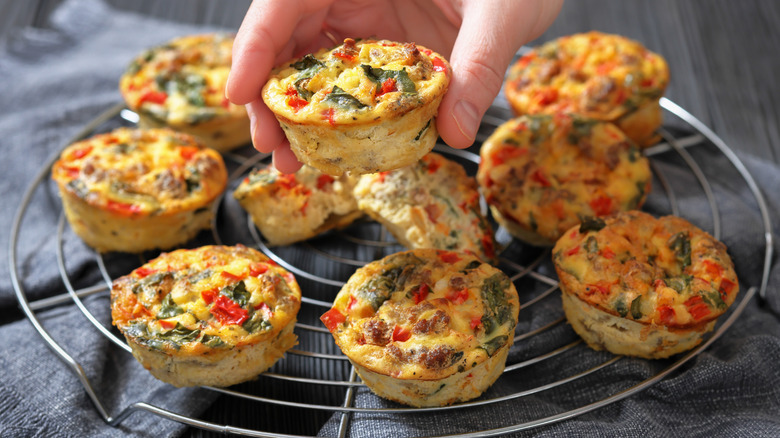 Savory vegetable muffins on wire cooling rack, with hand lifting one muffin up