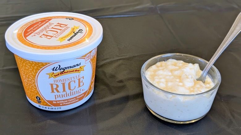 A plastic container of Wegmans rice pudding next to a glass bowl of pudding with a spoon in it