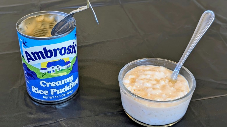 An open can of Ambrosia rice pudding next to a glass bowl of rice pudding with a spoon in it