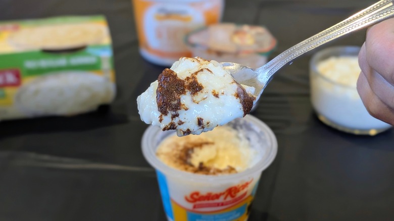 A close-up of a spoon of rice pudding with blurred packages of rice pudding in the background
