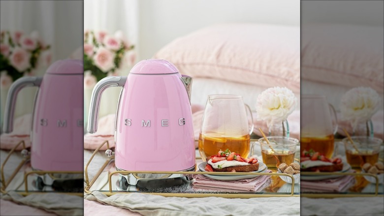 Pink Smeg electric kettle next to pitcher of tea and slice of cake on tray