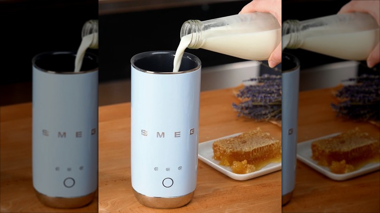 Hand pouring milk into Smeg mini milk frother on wooden table