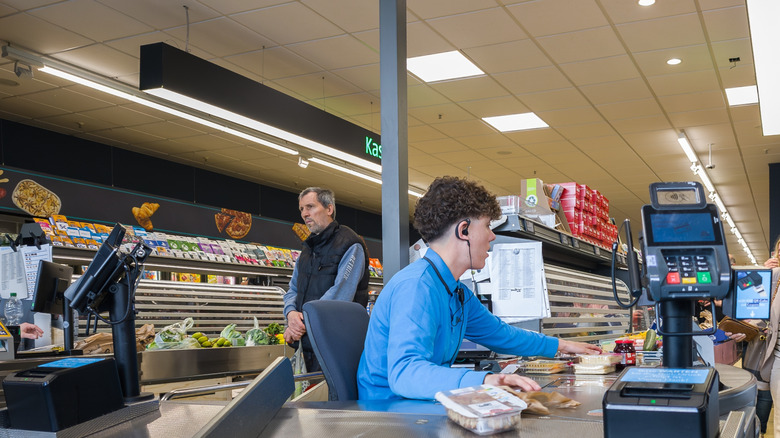 ALDI supermarket cashier scanning groceries at checkout with customers in queue
