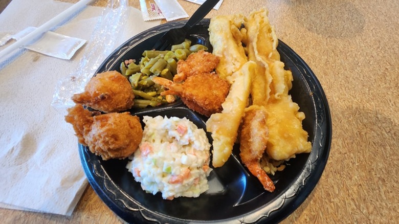 A plate of fried seafood, green beans, and coleslaw on a black plastic plate