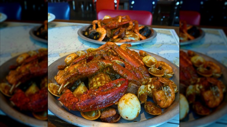 Seasoned crab legs, shrimp, corn, and potatoes on a black plate at a restaurant