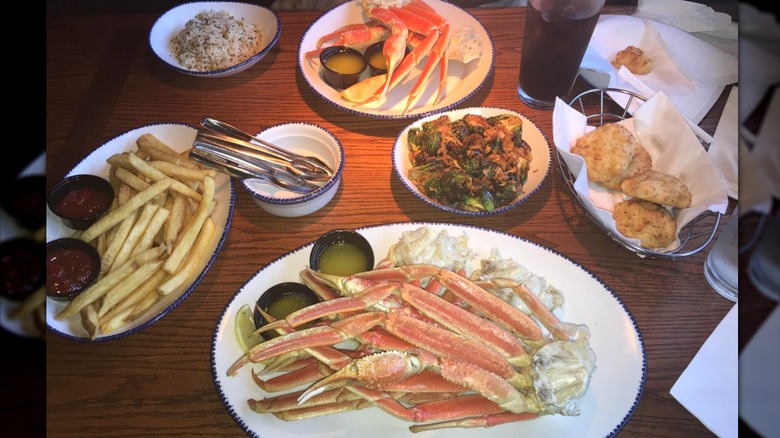 Plates of crab legs, fries, biscuits, and side dishes on a brown table
